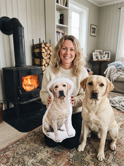 Kvinna vid braskaminen med sin labrador och kudden av samma hund